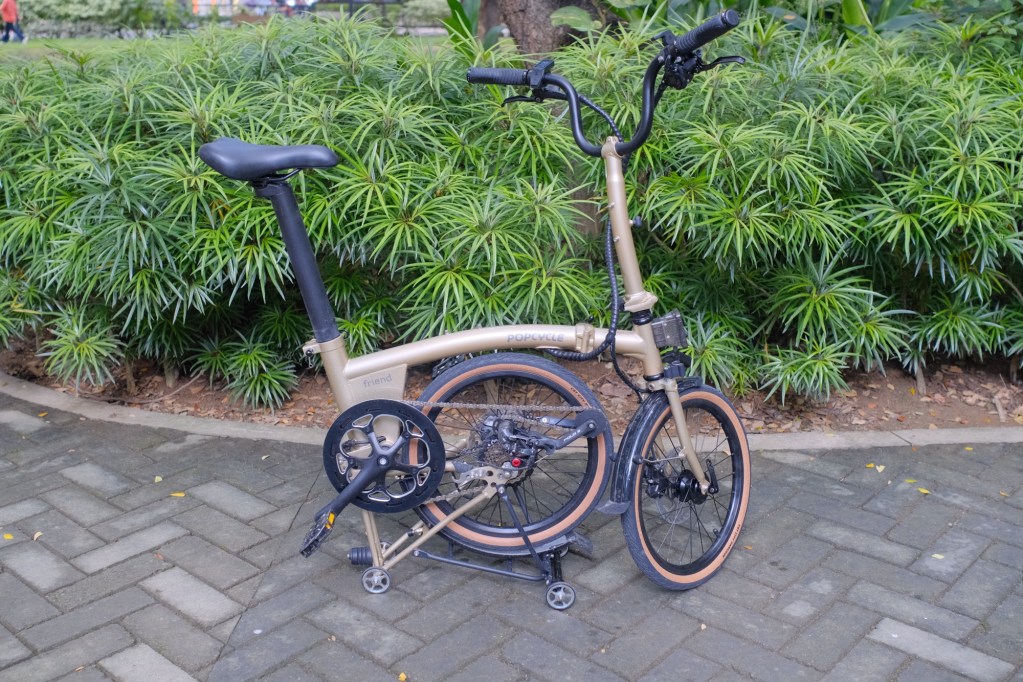 A folded bicycle with a sleek design, positioned on a paved path surrounded by lush greenery.