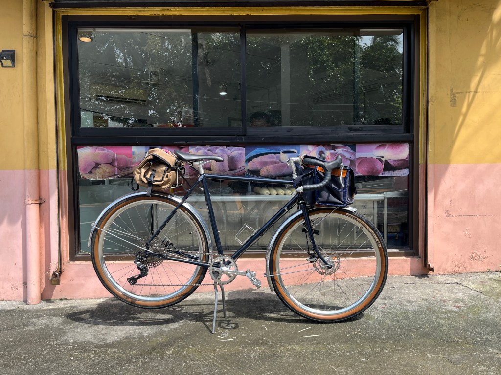 A bicycle parked next to a shop window in Barangay Kapitolyo, displaying baked goods, with colorful wall paint in the background.